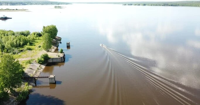 Aerial view of ship floating the river Kama, Perm krai, Russia. Motorboat and rural landscape from above, water waves, trees on the bank, summer sun day. Boat sailing on river. Top view.