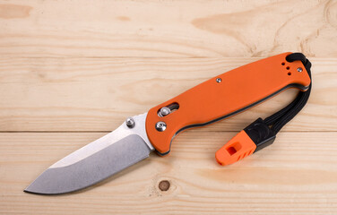 Rescue and survival folding knife and whistle on wooden background.