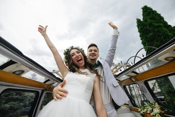 Hipster bride and groom rejoice in their retro bus on the background of an open hatch.