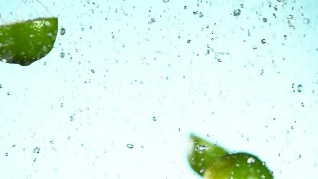 Super slow motion of lime pieces collision with water splashes, white background. Filmed on high speed cinema camera, 1000 fps.