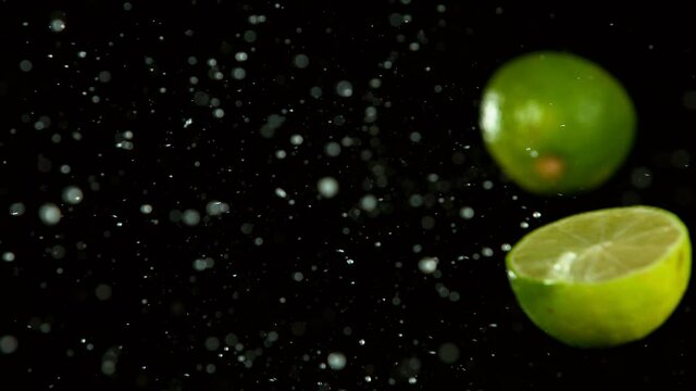 Super slow motion of lime pieces collision with water splashes, black background. Filmed on high speed cinema camera, 1000 fps.