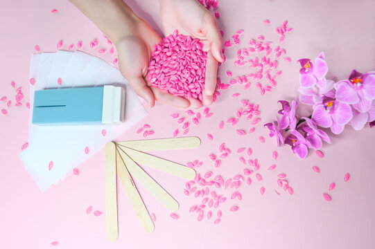 Set of depilation and beauty on pink background concept - sugar paste or hair removal waxing melted paste and stripes, orchid and female hands. Film Wax Granules or hot wax, cartridge, wooden spatula.