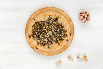 sunflower and pumpkin seeds lie on a round wooden plate, next to garlic cloves on a white wooden background. Organic healthy, vegetarian immune natural products, top view.