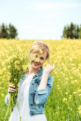 Naklejka na ściany i meble Happy girl in a field with a bouquet of flowers.Yellow rapeseed field.Freedom, happiness and the idea of conception