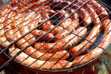 Pork and chicken sausages. Cooking on barbecue chargrill, brazier. Top view, closeup. Outdoors. Fast food. Preparation of sausages on outdoor charcoal grill.