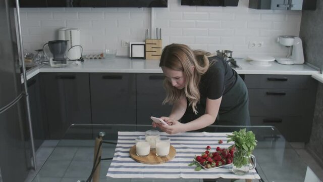 Confectionery blog. Woman in black shirt photographing Panna Cotta with orange