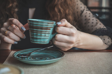 Vintage hand photo of the girls who lifted an elegant ceramic cup covered with a pattern of colored circles over a saucer