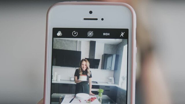 Confectionery blog. Someone takes photos on woman in black shirt with cake decorated with strawberry.