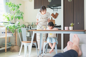 Fototapeta premium キッチンでお絵かきをする女の子と、料理をしながら見守る母親