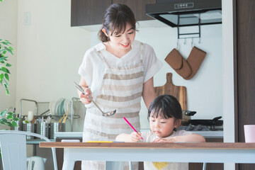 キッチンでお絵かきをする女の子と、料理をしながら見守る母親