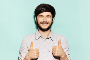 Studio portrait of young smiling guy showing thumbs up on background of aqua menthe color.