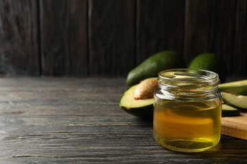 Board, avocado and oil on wooden background, space for text