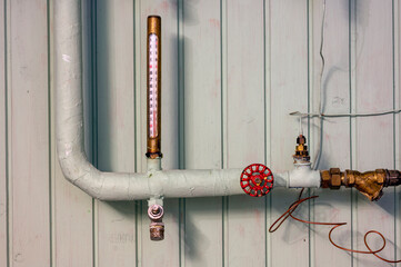 thermostat and pipes at a wooden wall in a basement