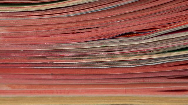 Closeup view video footage of stack of many old paper magazines. 
