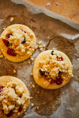 homemade buns with fruit and crumble on white baking paper ready for baking in the oven.