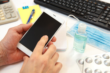 Smartphone in hands on the background of the workspace in the office.
