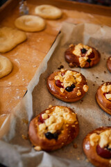 golden, homemade buns with fruit and crumble on white baking paper. in the background buns ready for baking in the oven.
