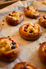 Freshly baked buns with fruits and crumble on white baking paper.