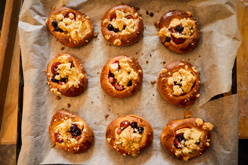 Freshly baked buns with fruits and crumble on white baking paper.
