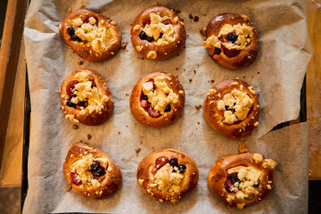 Obraz na płótnie Canvas Freshly baked buns with fruits and crumble on white baking paper.