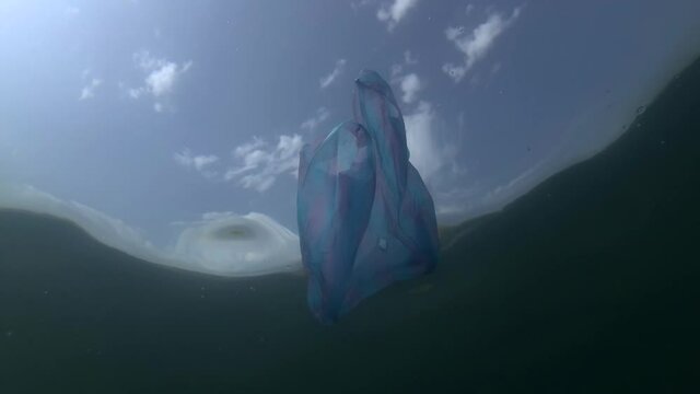 Plastic pollution, blue bag and school of Sand Smelt swims underwater on background blue sky with clouds. Low-angle shot. Plastic debris underwater. Plastic garbage environmental pollution problem