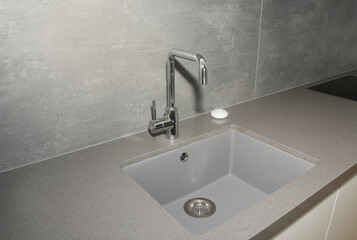 A close-up on undermount enameled cast iron single basin gray kitchen sink with a stainless steel kitchen faucet against gray wall.
