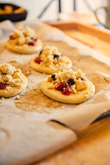 homemade buns with fruit and crumble on white baking paper ready for baking in the oven.