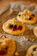 homemade buns with fruit and crumble on white baking paper ready for baking in the oven.