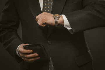 Businessman checks time looking at wristwatch holding expensive leather wallet in his hand. Close up shot. Deadline concept. Toned image.