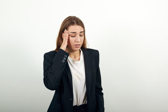 Headache grimacing pain holds the back of neck indicating location. Fatigue during workaholism labor. Young attractive woman with brown hair in a light t-shirt and black jacket on white background