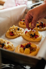 a woman's hand puts crumble on fresh buns with fruit, ready to bake in the oven.