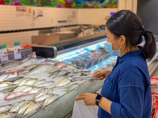 Young woman wearing medical face mask buying fish at groceries