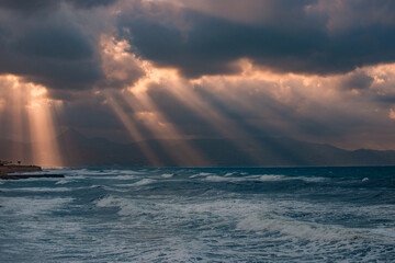 Naklejka premium sunset over the sea with rays of light between storm clouds