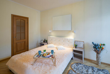Modern light interior of bedroom in apartment. White bed and bedsides. Breakfast on a tray.