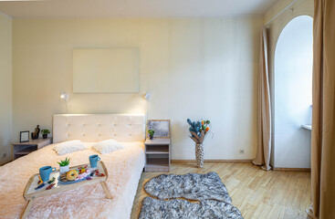 Modern light interior of bedroom in apartment. Front view of white bed and bedsides. Breakfast on a tray.