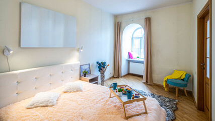 Modern light interior of bedroom in apartment. Cozy bed. Tray with food. Arch window.