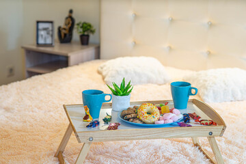 Close-up of tray with breakfast on the bed. Romantic composition. Couple of mugs, sweets and donut.