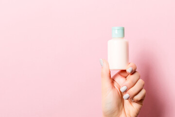 Close up of female hand holding a bottle of cosmetics product at pink background with copy space