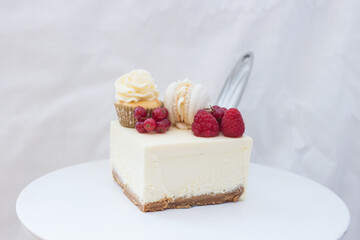 Slice of classic vanilla cheesecake New York with fresh raspberry and red currant on white cakestand.