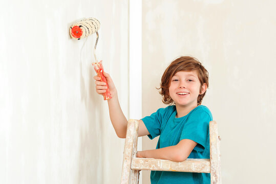 Boy paints the wall with a roller. Home renovation. Kid using paint roller.