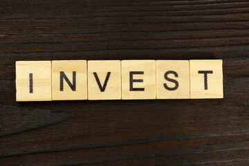 Fototapeta premium Invest word of square letters on a dark wooden background