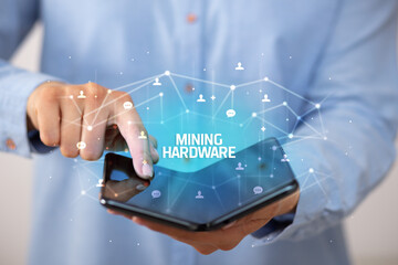 Businessman holding a foldable smartphone with MINING HARDWARE inscription, new technology concept