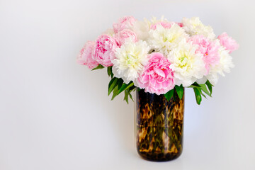 Pink peony flowers in leopard pattern glass vase, white background with a lot of copy space for text. Feminine floral composition. Close up, top view, backdrop, flat lay.
