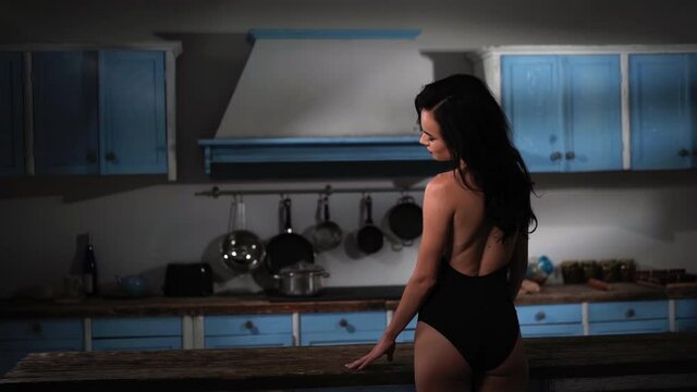 Pretty sexy fashion woman posing on kitchen dressed in bodysuit lingerie. Cheerful sexy woman sits on countertop in old vintage kitchen. Sensual woman in sexy lingerie. Prores 422.