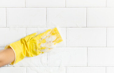 A female hand in a yellow latex glove sponges a tile. There is a lot of foam in the sink. The concept of cleaning the bathroom or kitchen, cleanliness. Copyspace.