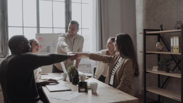 Businesspeople putting their fists on top of each other on the desktop in nice light workstation, wearing casual clothes. Conception of successful team-building