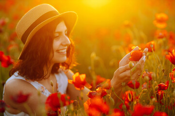 Beautiful girl in the poppy field. Portrait of a cute brunette girl in poppy field at sunset in a white dress and hat. Summertime.