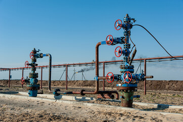 Fototapeta na wymiar Petroleum well wellhead equipment. Hand valve with handwheel on the flow line. Oilfield site. Oil, gas industry concept. Industrial site background. Production oil. Multiple check valve gate armature.