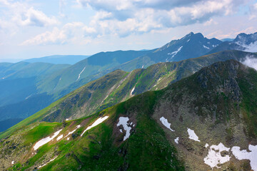 Fototapeta premium stunning landscape in high mountains of romania. grass and spots of snow on the slopes. rocky peak in the distance. clouds on the sky