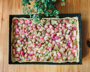 The process of making rhubarb pie. Sliced ​​rhubarb is laid out on the dough in a baking dish. Pie filling. Wooden table.